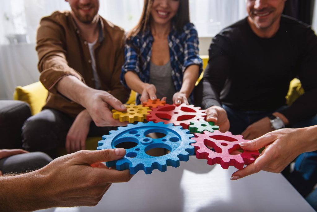 Project manager and Scrum Master inspiring Agile team members to work as a team holding colorful wheel-shaped puzzles