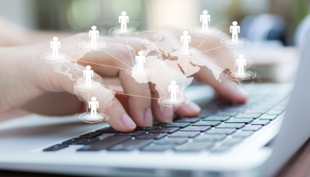 An online manager's hands typing on a laptop behind a virtual world map sitting at his home office and working remotely