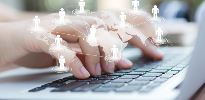 An online manager's hands typing on a laptop behind a virtual world map sitting at his home office and working remotely