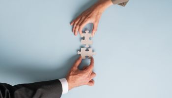Collaboration works for your company as two businessmen put two wooden pieces of a puzzle together demonstrating collaboration