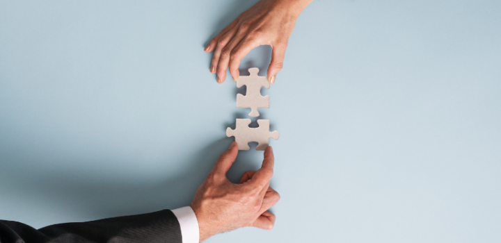 Collaboration works for your company as two businessmen put two wooden pieces of a puzzle together demonstrating collaboration