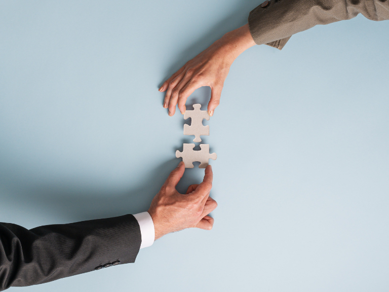 Collaboration works for your company as two businessmen put two wooden pieces of a puzzle together demonstrating collaboration