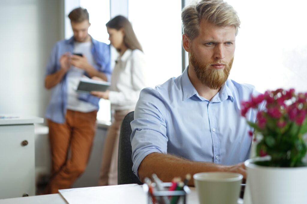 young male blonde employee has problems after level 10 meeting using easynote to help him in his office with two coworkers behind him 