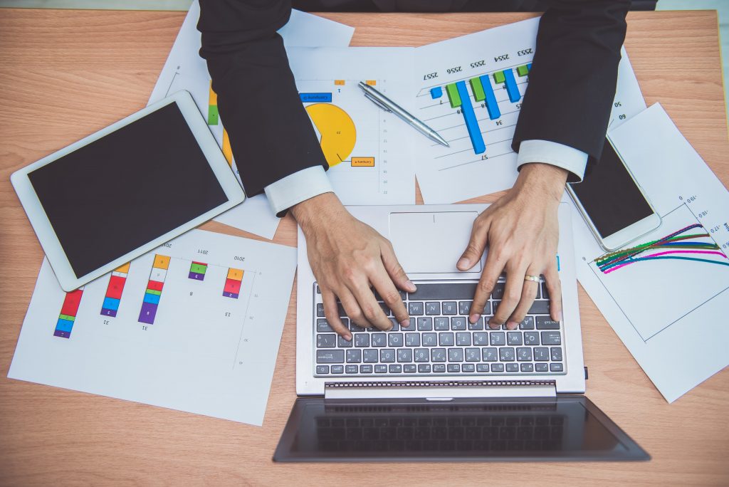 A finance employee using budget dashboards on paper and transferring data to the virtual budget dashboard on the company laptop in an office