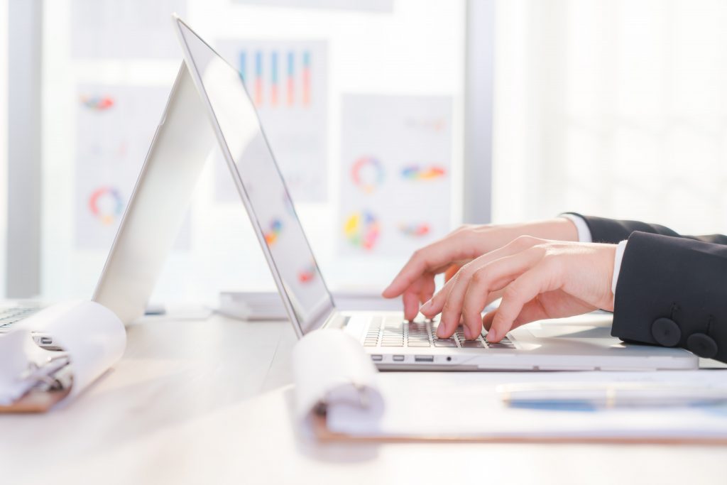 Closeup of online manager's hands typing on a laptop while looking at online manager courses and using Easynote to organize time.