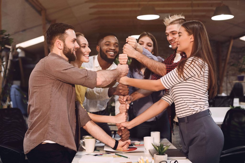 Scrum team members standing together and holding hands on top of each other's hands using scrum techniques with scrum master