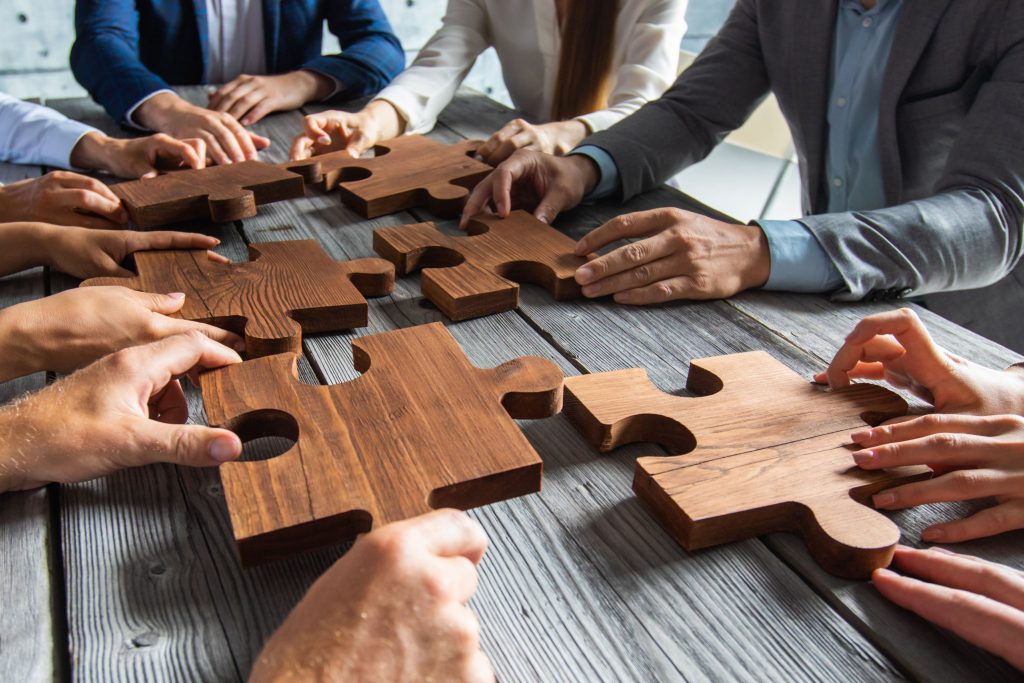 What techniques could scrum masters use? Scrum team holding wooden puzzle pieces representing teamwork and collaboration.