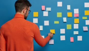 planning tips used by a young male employee using stick it notes on a blue wall