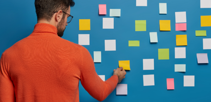 planning tips used by a young male employee using stick it notes on a blue wall