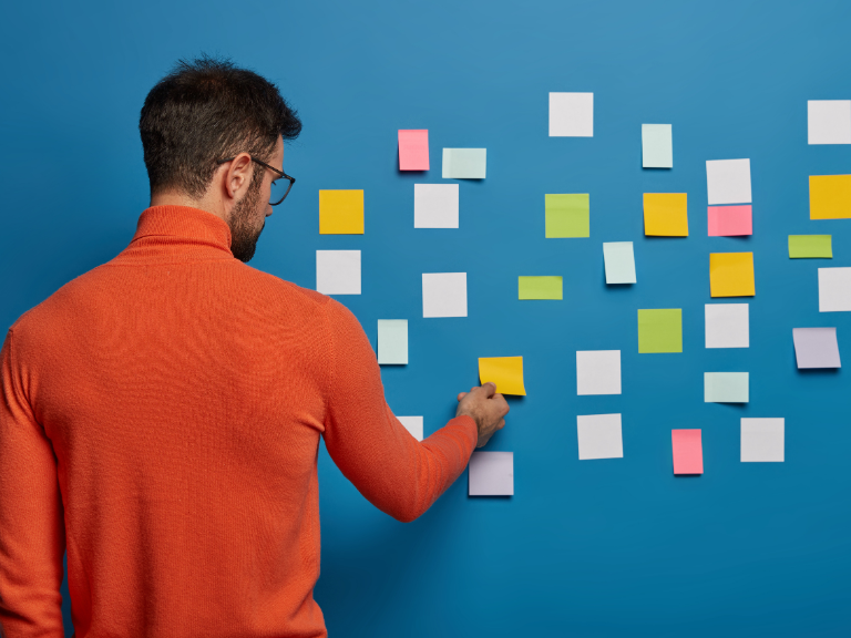 planning tips used by a young male employee using stick it notes on a blue wall