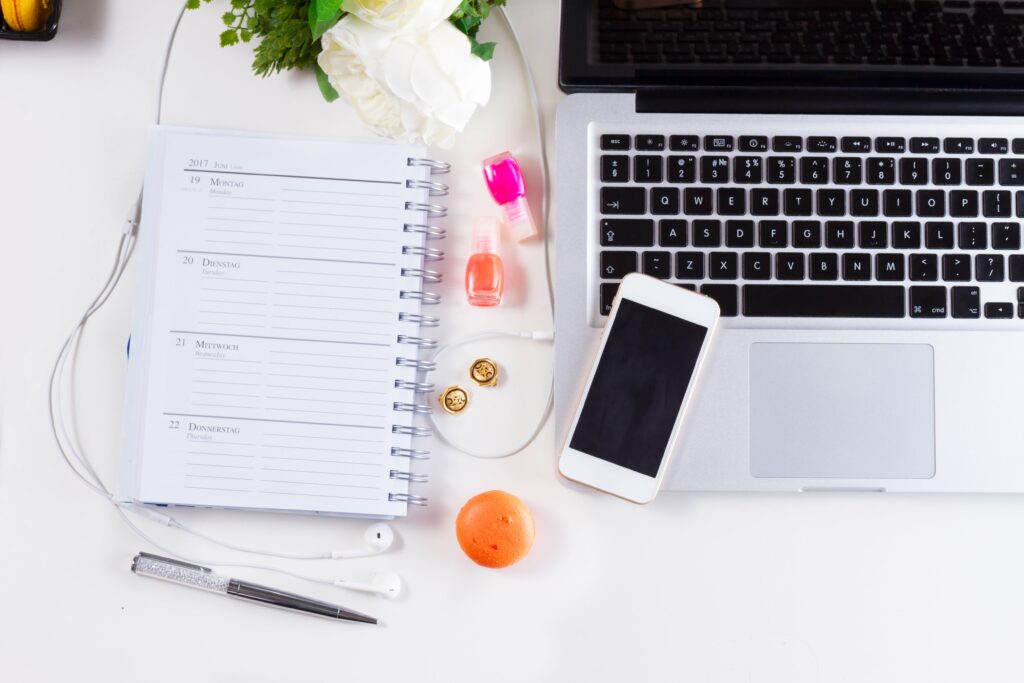 notebook and digital planner shown on a white desk which can serve as your hourly planner option